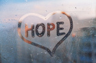 A drawing of the word hope inside a heart on a foggy window